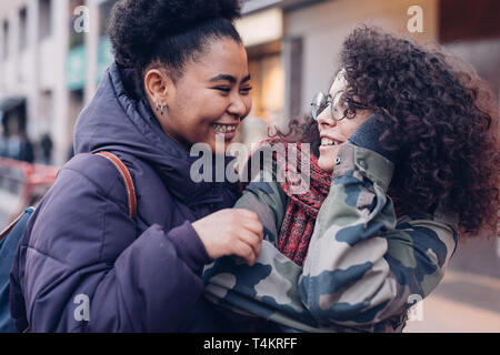 Deux jeunes femmes serrant dans la rue avec des cheveux bouclés - amitié ; de la bonne humeur ; joyeux ; Banque D'Images