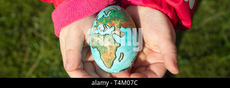 Enfant tenant un œuf avec la planète Terre peint sur elle lors d'une journée ensoleillée à l'extérieur. Banque D'Images