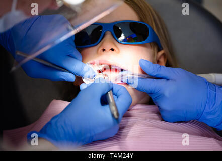 Effectuer la procédure de remplissage dentaire dentiste à une petite fille dans une clinique dentaire pédiatrique avec une aide de l'assistant. Calme enfant est assis dans un cabinet dentaire ch Banque D'Images