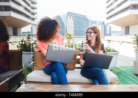 Deux femmes d'affaires à l'aide d'un ordinateur portable tout en grillage avec bière à la fin de la journée Banque D'Images