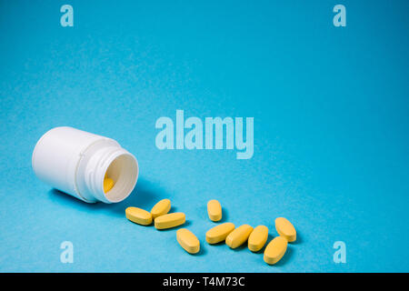 Bouteille blanche avec du jaune comprimés de vitamines. Médical pharmaceutique comprimés, comprimés sur fond bleu. Contexte La médecine with copy space Banque D'Images