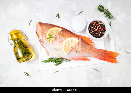 Matières premières poisson vivaneau et de tranches de citron, des herbes de romarin, sel et poivre sur fond blanc. L'alimentation saine et dieting concept. Ingrédients pour la cuisson sif Banque D'Images