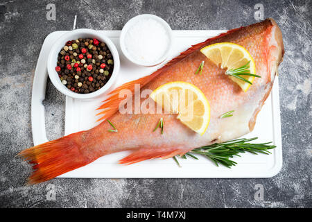 Matières premières poisson vivaneau et de tranches de citron, des herbes de romarin, sel et poivre sur fond sombre. L'alimentation saine et dieting concept. Vue d'en haut Banque D'Images