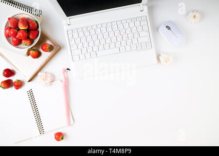 Espace de travail avec ordinateur portable télévision lay, tasse de café, des fraises, des accessoires et de fleurs sur fond blanc. Vue de dessus Offres de travail à la maison. Copy space Banque D'Images