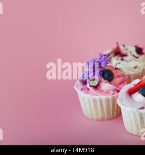 Ensemble de petits gâteaux délicieux avec des obturations et crème. Trois muffin avec de la crème sur un fond rose, copiez l'espace. Banque D'Images