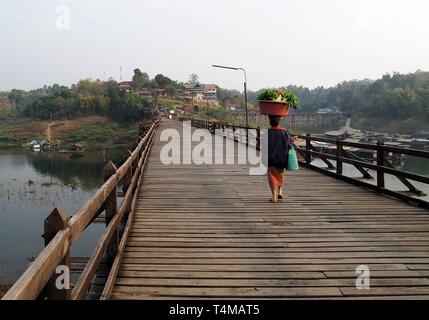 Une femme transportant certaines marchandises sur sa tête tout en marchant sur un pont en bois dans une région rurale en Asie. Banque D'Images