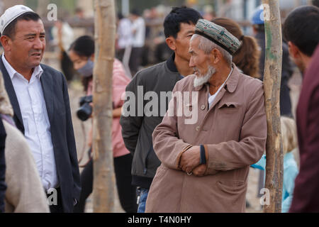 Homme barbu avec un doppa ouïghour traditionnelle (hat) s'appuyant sur un pôle à Kashgar Marché des animaux (Province du Xinjiang, Chine) Banque D'Images