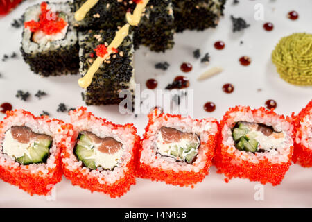 Close up of Philadelphia, décoré de rouleaux uramaki, Mayo et sauce wasabi. Deux types de rouleaux de sushi, rempli de salami, de concombre et de fromage à la crème, recouvert de tobiko rouge corail. Banque D'Images