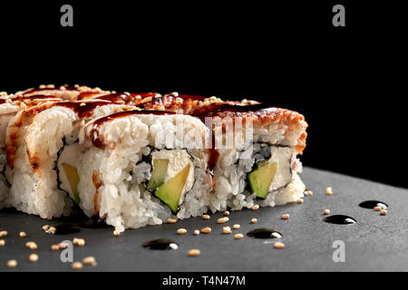 California roll close up. Sushis délicieux rempli d'anguille fumée, d'avocat et de fromage à la crème, sauce unagi topping, décoré avec du sésame. La plaque d'ardoise. Banque D'Images