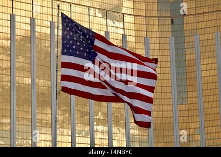 Un drapeau américain dans le vent souffle en face d'un haut bâtiment de verre jaune. Banque D'Images