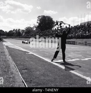 Années 1960, historique, sport automobile à Crystal Palace en circuit de course Crystal Palace Park dans le sud de Londres, Angleterre, Royaume-Uni. Un commissaire de course par la ligne d'arrivée de la piste avec le drapeau à damier a soulevé que la voiture gagnante est la dernière droite en face de la foule. Ouvert en 1927 pour les motos, c'était 1937 quand 20 voitures est entré le premier Grand Prix de Londres. Plus tard cette même année, la BBC broadacst la toute première course de moto télévisé du circuit. La dernière réunion a été en 1972 où il a été estimé que racing autour d'un parc à des vitesses de plus de 100 mi/h n'était pas sécuritaire. Banque D'Images