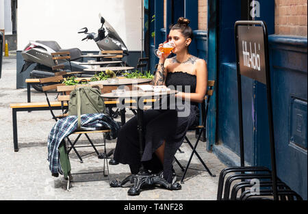 Jeune femme tatouée attrayante lisant un livre de poche et buvant de la bière dans un café-terrasse à Séville, en Espagne