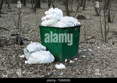 Old rusty metal green poubelle pleine de déchets plastiques debout dans parc de la ville ou la forêt. La pollution de l'environnement. Banque D'Images
