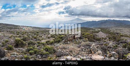 Vue panoramique de la grotte Shira Camp site sur la Machame à vélo sur le mont Kilimandjaro, en Tanzanie. Le Mont Meru est derrière les rayons du soleil en arrière-plan. Banque D'Images