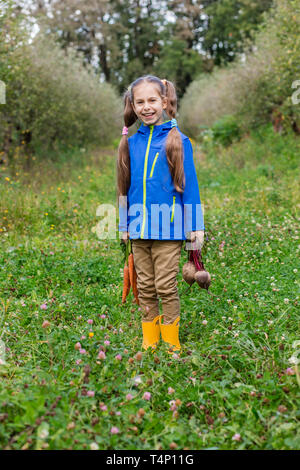 Cute girl holding carottes et betteraves en mains juste pour recueillir dans le jardin. Les légumes fraîchement récoltés. Banque D'Images