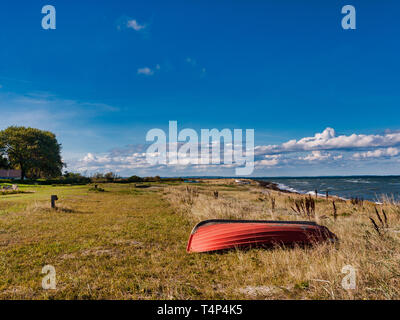 Bateau rouge est allongé sur une prairie sur la plage de la mer Baltique contre un ciel bleu avec des nuages sur l'île de Langeland, Danemark Banque D'Images