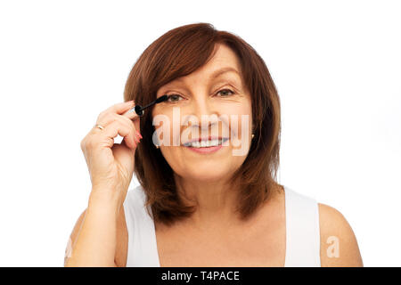 Beauté, maquillage et les vieux concept - young woman applying mascara pour cils sur fond blanc Banque D'Images