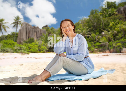 Les gens et l'été concept - happy smiling woman sitting on serviette sur fond de plage tropicale de l'île des Seychelles Banque D'Images