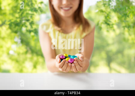 Pâques, les vacances et les personnes concept - close up of happy girl holding des oeufs en chocolat d'aluminium colorés sur fond naturel vert wrappers Banque D'Images