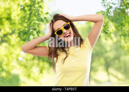 L'été, l'accessoire et du concept de personnes - jeune femme ou adolescente en jaune t-shirt et lunettes de soleil pour tenir sa tête sur bac naturel vert Banque D'Images