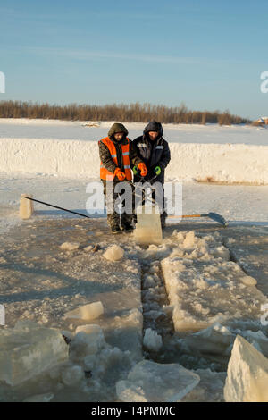 Tirez le bloc de glace travailleurs hors du trou avec des pinces en acier Banque D'Images