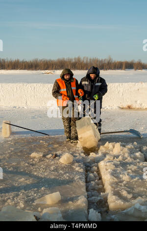 Tirez le bloc de glace travailleurs hors du trou avec des pinces en acier Banque D'Images