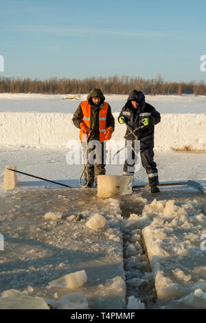Tirez le bloc de glace travailleurs hors du trou avec des pinces en acier Banque D'Images
