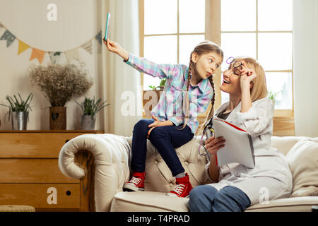 Avoir du plaisir avec un médecin. Cheerful pretty cute 8-years-old girl avec de longues tresses brunes s'amuser tout en faisant vos autoportraits avec charmant lumineux agréable Banque D'Images