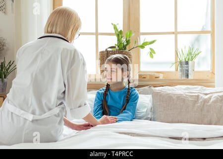 Doctor putting kid au lit. Bon-blonde attrayant attrayant agréable mid-adult pédiatre dans un manteau blanc mettre à poil long cute peu mauvais gi Banque D'Images