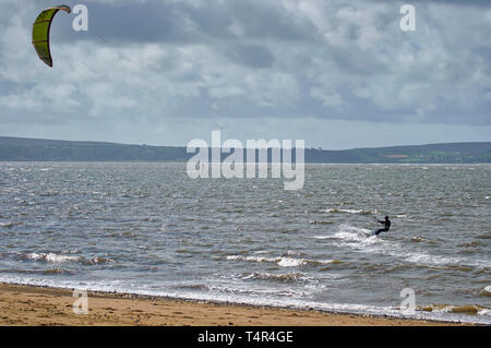 Un kite surfer faire son chemin le long de la plage de Llanelli avec la péninsule de Gower en arrière-plan, sur un matin d'été venteux à Llanelli, Galles du Sud. Banque D'Images