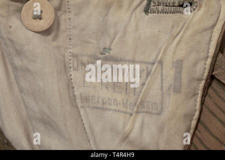 Une combinaison uniforme de camouflage veste doublée avec marsh fait de gros drap de laine, hiver/été réversible, double-breasted, avec le capot. Dans la partie inférieure deux poches à rabat de chaque côté, pas de timbre. Matériel pantalon comme avant, une poche latérale de chaque côté, avec plusieurs liens de serrage, l'élastique avec poinçon 'Uniformwerke F.Reitz Antwerpen-Merksem" ainsi que la taille '1'. Livré avec une paire de mitaines, estampillé avec RB nombre, et un capot supplémentaire ainsi qu'un camouflage réversible pour couvrir le casque d'acier (chaque sans timbre). Avec raccommode, des signes de vieillissement et d'utilisation. hist, Editorial-Use-seulement Banque D'Images