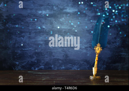 Ancienne plume stylo plume verte avec inkwell plus de bureau en bois en face de l'arrière-plan de mur noir. Vintage style ancien et filtrés. Photo conceptuelle sur l'hi Banque D'Images