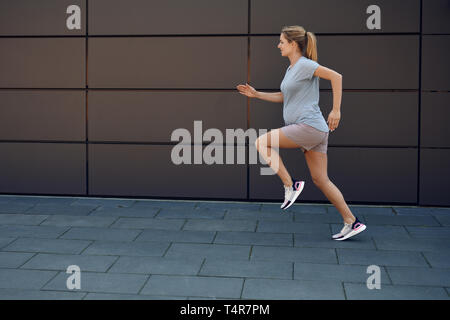 Jeune femme enceinte keeping fit courir le long d'un trottoir pavé en face d'un mur urbain dans un concept de vie sain Banque D'Images