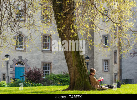 Royal Mile, Édimbourg, Écosse, Royaume-Uni, 18 avril 2019. Météo France : Un homme est assis au soleil, appuyé contre un arbre, lisant un livre en Cour Chessels Banque D'Images