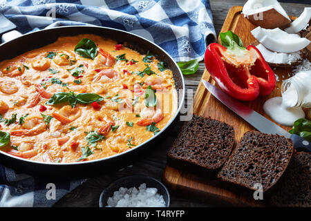 Crevettes en sauce Coco mélangé avec des légumes dans une poêle sur une table en bois rustique avec des essuie-tout et les ingrédients, camarao pas de leite de coco, b Banque D'Images