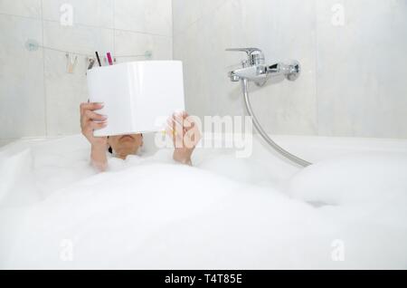 Femme lisant un livre dans une baignoire avec de la mousse Banque D'Images