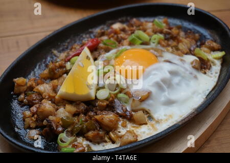 Porc délicieux grésillantes sisig nourriture philippine de porc haché avec l'oeuf cru chaud cuisson sur bac pot en argile avec tranche de citron frais et piments rouges cuisine Asiatique Banque D'Images