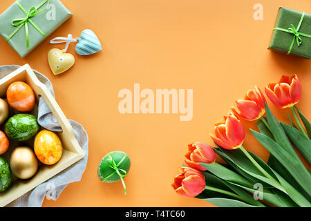 Mise à plat de Pâques sur papier orange avec copie-espace. Les oeufs peints dans le bac décoratif, printemps tulipes, coffrets cadeaux et décorations coeur. Banque D'Images