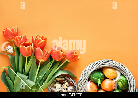 Mise à plat de Pâques sur papier orange avec copie-espace. Oeufs de cailles au nid d'oiseau, printemps tulipes, enveloppe et décorations florales Banque D'Images