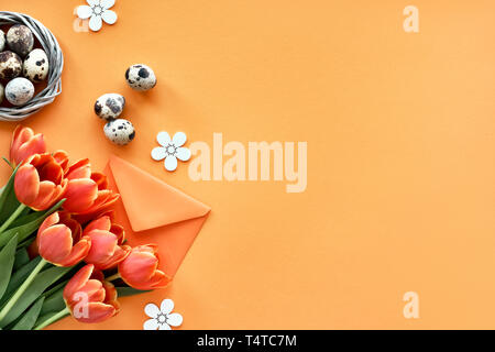 Mise à plat de Pâques sur papier orange avec copie-espace. Oeufs de cailles au nid d'oiseau, printemps tulipes, enveloppe et décorations florales Banque D'Images