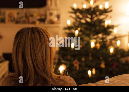 La femme est assise sur un canapé en face de l'arbre de Noël, vue arrière Banque D'Images