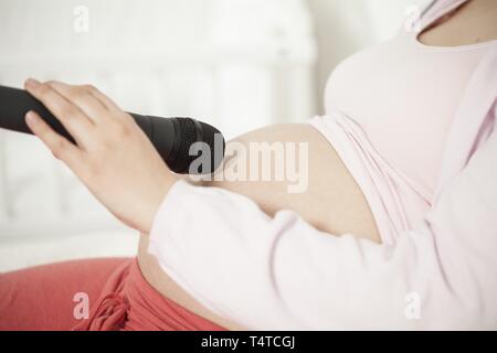 Pregnant woman holding micrphone sur ventre Banque D'Images