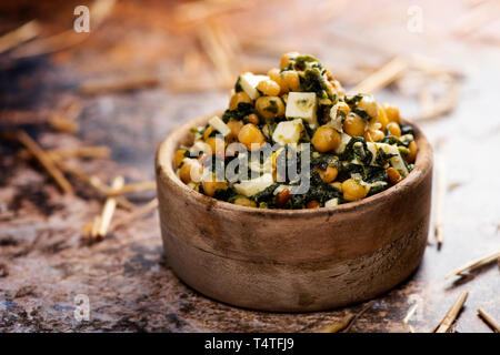 Une salade de pois chiches, avec les épinards, les pignons, l'oignon et fromage, servi dans un bol en buis rustique, placée sur une table rustique Banque D'Images