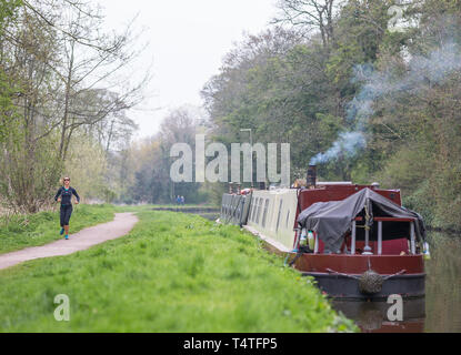 Bateau à rames avec cheminée fumée amarrée le long du canal britannique avec une coureuse (vue de face) jogging le long du chemin de halage du canal. Banque D'Images