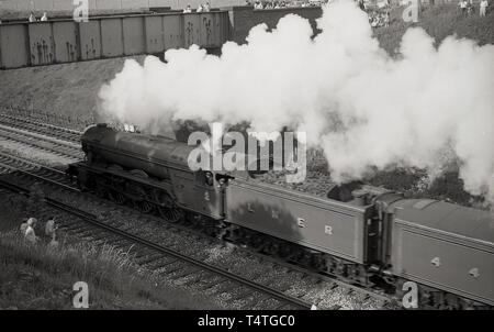 1969, historique, sur un pont et une grassbank, regarder les gens comme la célèbre locomotive à vapeur, le Flying Scotsman', va passé, England, UK. Banque D'Images