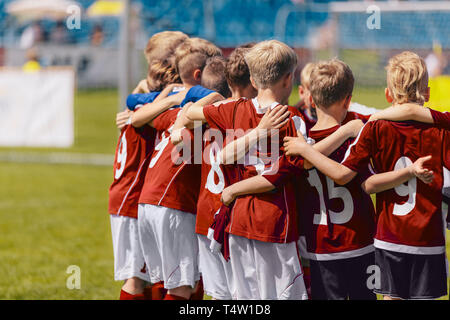 L'équipe de soccer l'entassement. Les enfants en rouge sportswear se tenant ensemble et à l'écoute de coach. Tournoi de soccer match de football junior Banque D'Images