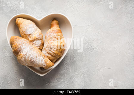 Des croissants frais de la plaque, comme coeur sur fond gris. Vue d'en haut. Copier l'espace. Banque D'Images