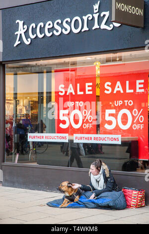 Femme sans-abri mendiant avec chien assis à l'extérieur de la boutique Accessorize à Cheltenham mendier au large de consommateurs et des passants au cours de la vente Janvier Banque D'Images