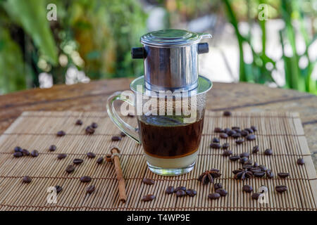 Rrd traditionnel vietnamien de café filtre avec lait concentré sucré dans un café de la rue. Les grains de café et le bâton de cannelle sur la table. Banque D'Images