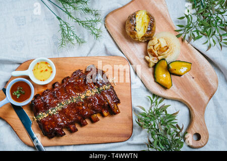 Côtes levées au barbecue avec du miel se trouve sur une vieille planche en bois vintage rustique, sauce, sauce de poisson, l'aneth, les oignons sur la table en haut, bas, angle shot Banque D'Images